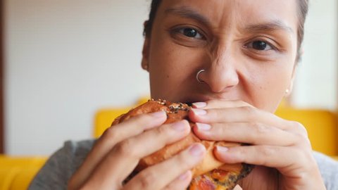 Young Hungry Woman Biting Vegan Meatless Burger in Fast Food Restaurant. Portrait of Angry Face Female Eating and Looking in Camera. 4K Slowmotion.