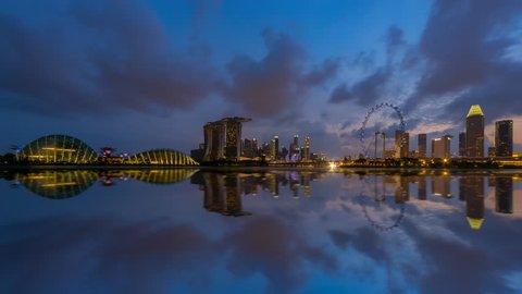Beautiful Time lapse of Day to Night of Marina Bay Sands area CBD in Singapore city skyline by a river at dusk with reflection. Pan down motion timelapse.