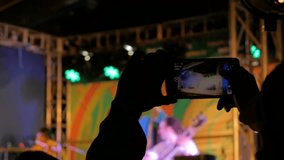 Unrecognizable hands silhouette taking photo or recording video of live folk music concert with smartphone at night. Photography, entertainment and technology concept