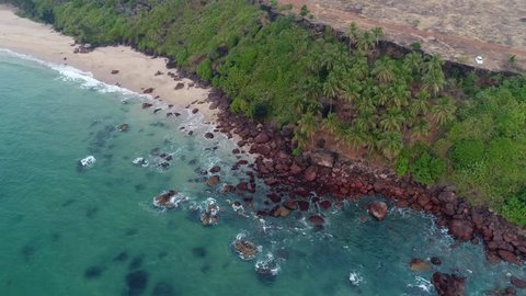 Aerial view. The ocean waves are washed by a steep bank covered with palm trees. Tropical bay of sea in Goa, India.
