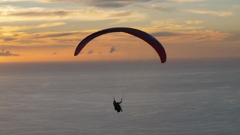 Paraglider makes a hard turn as he maneuvers the sky over ocean at dusk