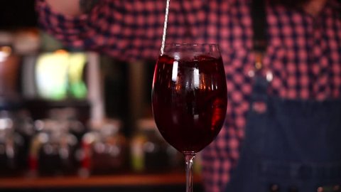Slow motion view on process of drink mixing alcohol cocktail in red wine glass, close up bartending