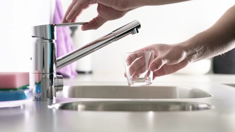 Man filling glass with tap water. Sink in home kitchen. Modern faucet. Person pouring fresh drink to cup.