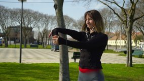 Beautiful concentrated sportswoman stretching hands in park. Attractive sporty girl in earphones exercising and looking away outdoor. Working out concept