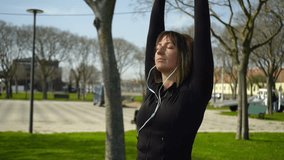 Focused sporty girl in earphones exercising in park. Slider shot of beautiful young sportswoman listening music and working out outdoor. Healthy lifestyle concept
