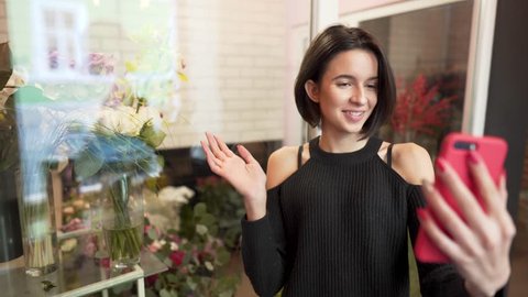 Beautiful slim thin hot sexy brunette in black shoulderless sweater filming herself on camera, doing story for instagram. Girl near flower shop