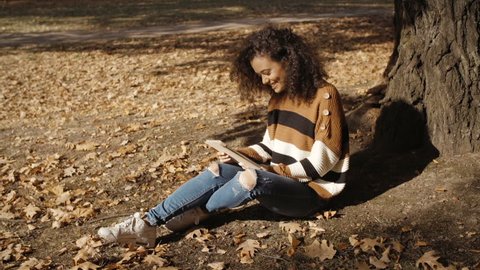 Beautiful young girl with dark curly hair using tablet computer, outdoor.