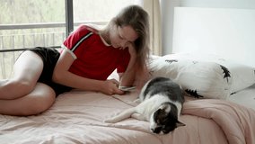 cute teen girl with pink hair plays on phone, then puts phone away and plays with cat on bed