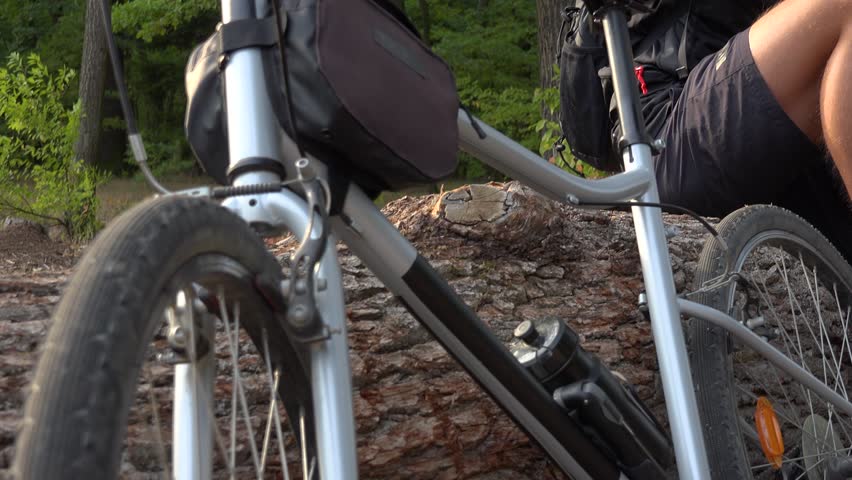A young handsome cyclist sits on a log next to his bike in a forest and smiles at the camera - view from below