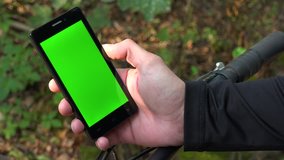 A cyclist looks at a smartphone with a green screen - closeup on the phone