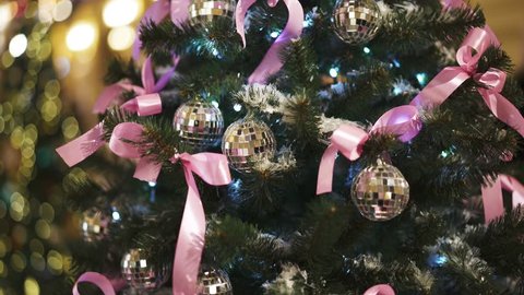 Gimbal tilt up shot of artificial christmas green tree with artificial snow decorated with silver balls, pink ribbons and long white garland