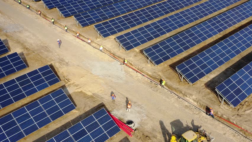 Aerial view of a big group of workers laying power cable at the giant industrial solar power station (solar electricity plant)  Royalty-Free Stock Footage #1025499572