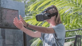 Testing new technologies. Attractive young woman in VR headset gesturing and smiling while sitting at home. Woman in VR headset looking at the hands in virtual reality.