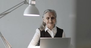 Business grandmother works at a laptop. An old woman with deep wrinkles talks on video on the computer in the office.
