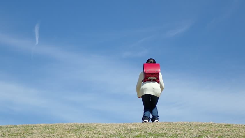 Japanese elementary school girl jumping in the blue sky(rear view)
