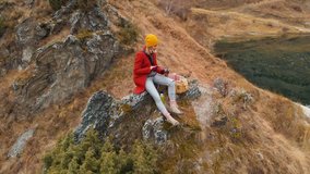 Aerial view of a girl sitting on a rock on a lakeside that takes a photo of the landscape on the phone and shoots a video. Travel video