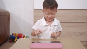 Cute little smiling Asian 2 - 3 years old toddler baby boy child sitting on floor watching a video from tablet pc. Kids playing with tablet computer, Gadget-addicted children concept