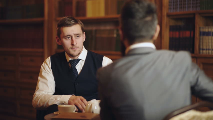 Professors speaking or discuss education in vintage interior. Intelligent elite and education concept. Men with antique bookshelves on background. Intelligent men, scientists spend leisure in library