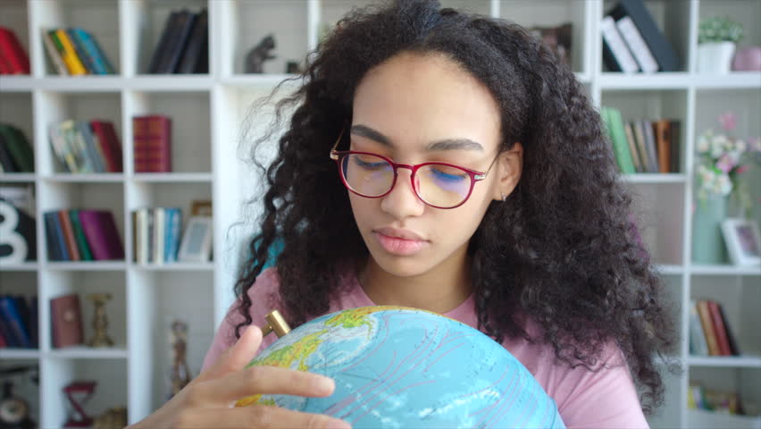 Beautiful african american female student spinning and watching the globe in her hands