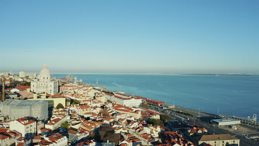 Aerial view; drone flight over the narrow streets of Portugal capital; panoramic landmark with last sunbeams; Alfama, with the churches of S. Vicente de Fora, Engrácia, and Estevao, Tagus river behind Royalty-Free Stock Footage #1025513300