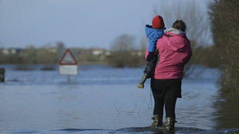 Classic shot of mother and child walking in flood water in front of flood sign