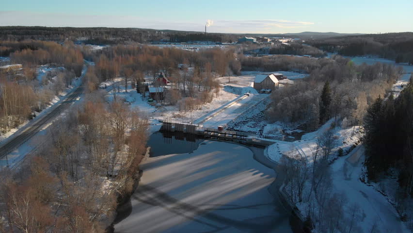 Drone footage flying over a river towards a dam and an old water power station with a forest in the background. Filmed in realtime at 4k.