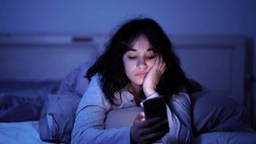 4K wide video of an Addicted young woman chatting and surfing on the internet using smart phone sleepy, bored and tired late at night. Dramatic dark light. In Internet, Mobile addiction and insomnia.