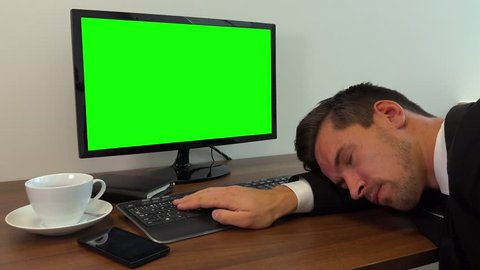 An office worker in a suit sleeps on a desk with a computer with a green screen - closeup