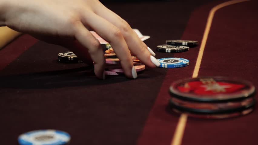Playing poker. Woman is nervous, fingering the chips in her hand on the poker table. Hand close up. Casino gamble.