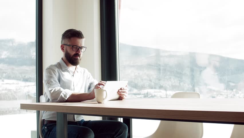 A mature man sitting at the table in new home, using tablet.