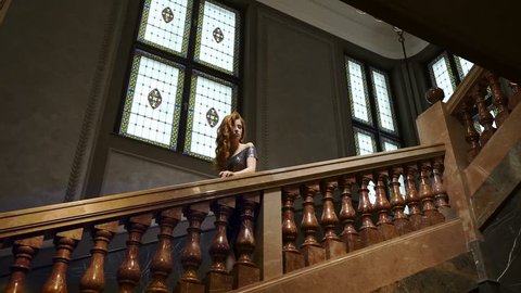 Elegant Young Woman Coming Down The Stairs. Decorative Railings In The Building. Tall French Windows.