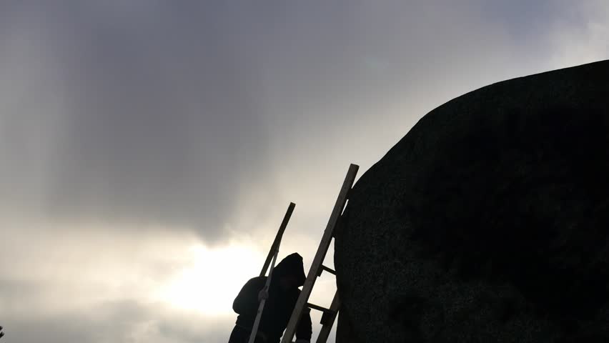 medieval man lifting Christan cross up to the rock top silhouette