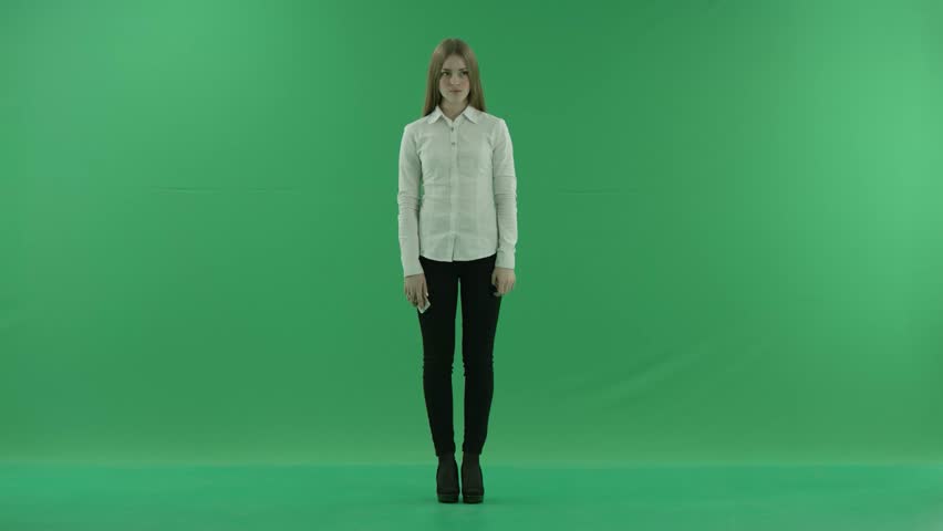 happy business woman is talking on her mobile phone and dansing as she has got god news. She wears formal dress: white shirt and blak trousers. Businesswoman smile over green screen standing fullength