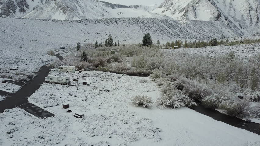 Drone flying alongside RV´s parked on a campsite in the snow, with a beautiful small river on the right side. Camper and RV life concept.