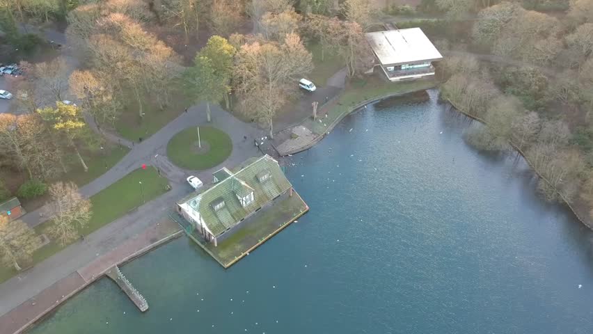 Aerial rotation around public park lake house as white birds fly around overhead.