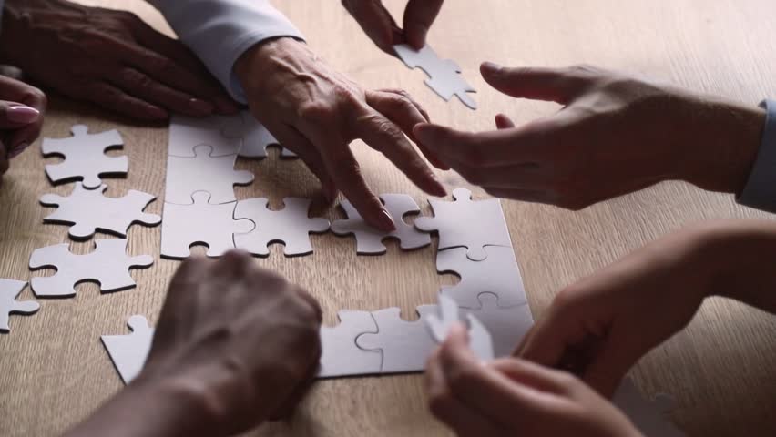 Diverse hands of business people connect puzzle pieces together on office desk, multi ethnic team engaged in finding solution, decision making collaborate in teamwork strategy concept, close up view