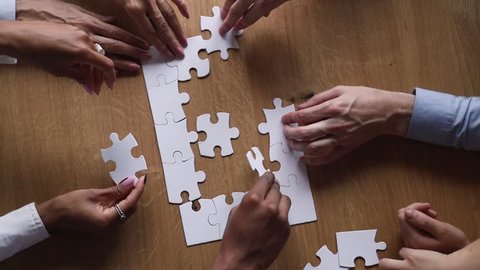 Hands of diverse business team people collaborate assemble puzzle together connect pieces at desk find common purpose solution engaged in help support contribute in teamwork concept top close up view
