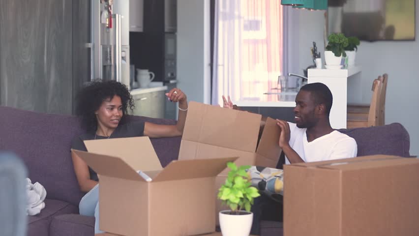 Happy child girl jump out of box give high five to dad play with black parents in living room, african family and kid daughter laughing having fun pack unpack enjoy relocation moving in new home Royalty-Free Stock Footage #1025577017