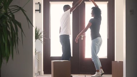 Happy african american couple first time home buyers dancing in hallway moving with boxes celebrate relocation buy new house, excited black family tenants renters having fun enjoy renovation mortgage