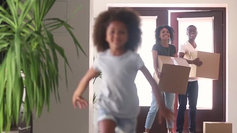 Happy black family moving in new home, excited african american parents and cute child daughter tenants owners holding boxes enter big house kid running in hallway, mortgage, relocation and welcome