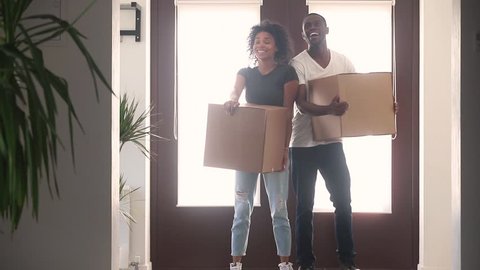 Happy black couple first time home buyers holding boxes talking embracing standing in hallway coming into big modern house, african american renters tenants relocating on moving day, family mortgage