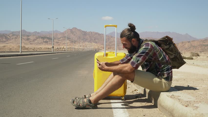 Handsome male traveler with luggage and rucksack using smartphone on highway 4k