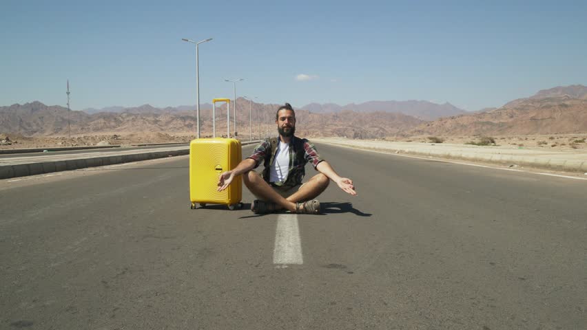 Portrait of young male traveler meditate on hihgway with yellow luggage 4k