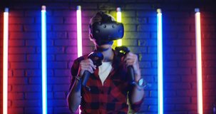 Close up of the Caucasian girl in VR glasses having virtual reality headset and playing a game like boxing with joysticks in hands. Colorful neon lamps background.