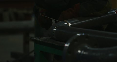 Welder in welding mask, in working clothes at the factory, welds the pipe in the factory room. Welder. Industry. Work at the factory. Pipe welding. Electrode. Melting. Welding works. Semi-automatic we