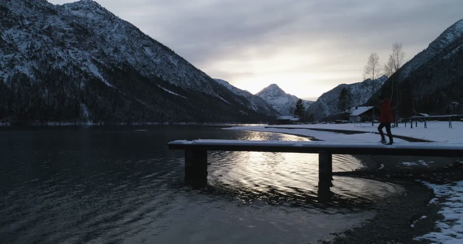 Person walks out onto jeti at Lake Plansee looking at sunset. Slow motion