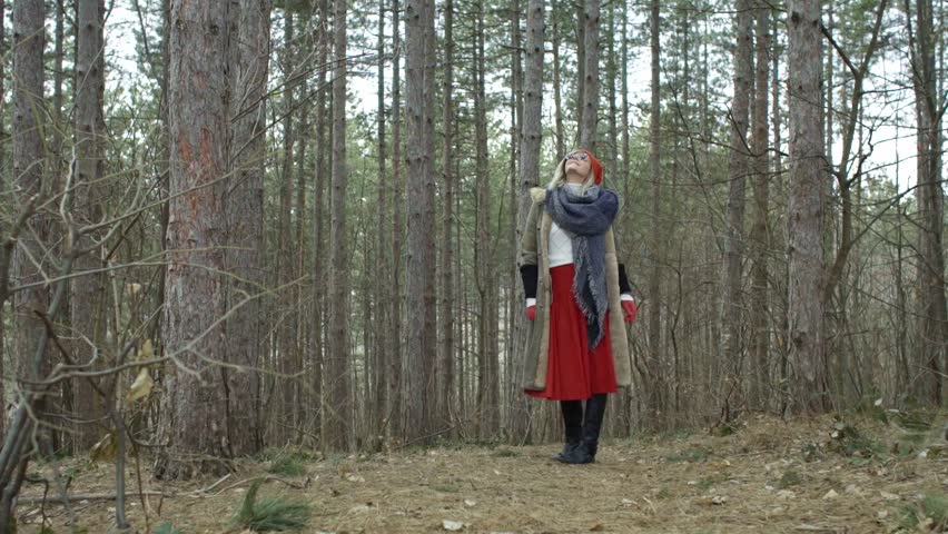 Young attractive woman with red hat and red skirt spinning around in trough thick forest. Female walking in forest in winter
