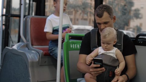 Dad riding in the bus with elder son and one year old baby daughter. Everyone watching fathers smart phone
