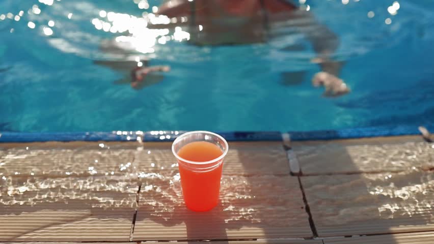Woman swims to the edge of swimming pool, takes fresh juice, drinks it and swims away, sunny day in the swimming pool outdoors, relaxing in the pool, water treatments