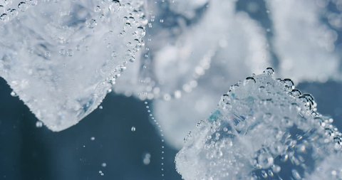 Slow motion macro of ice cubes immersing with splashes in cold fresh water. Shot in 8K.